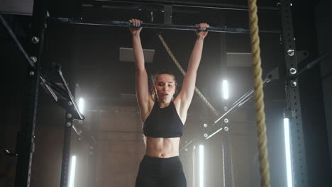A-sporty-young-woman-pulls-herself-up-on-a-horizontal-bar-in-a-dark-gym-in-a-beautiful-neon-backlight.-Endurance-and-perseverance-in-pulling-up-movement-towards-the-goal
